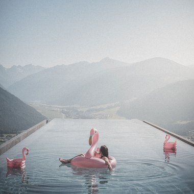 Alpenreych & Hubertus Park Relaxed person on flamingo float in infinity pool with mountain view