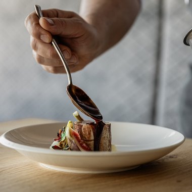 Ein Blick in unsere Weinkarte Koch gießt Soße über ein kleines Stück Fleisch auf einem weißen Teller