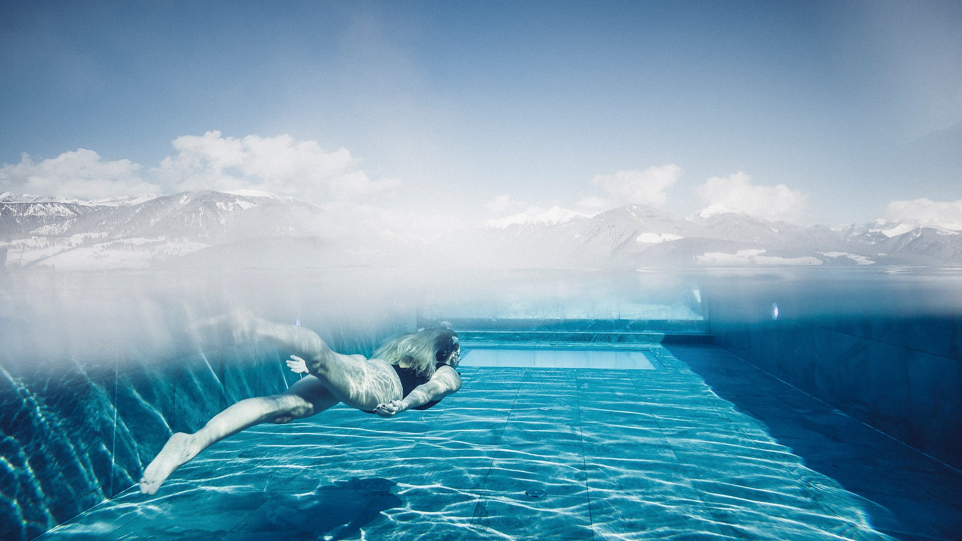 Our wellness hotel in Val Pusteria for relaxation seekers Woman swimming underwater in a pool with mountain view in the background