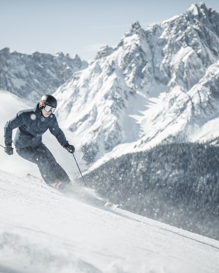 Unser Hotel in Olang zwischen Himmel und Erde Skifahrer fährt einen schneebedeckten Berg mit schroffen Gipfeln im Hintergrund hinab