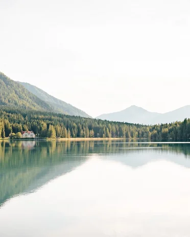 Current news and stories from Olang Mountain lake with reflected trees and a house on the shore